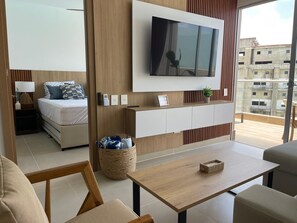 Ein modernes Hotelzimmer mit Bett, Wand-Fernseher, kleinem Tisch und Blick auf die Stadt.