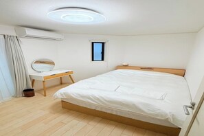 Ein Schlafzimmer mit Bett, Schreibtisch, Fenster und Klimaanlage.