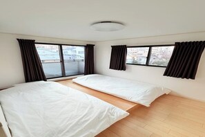 Ein Zimmer mit zwei Betten, großen Fenstern und Blick auf Gebäude.