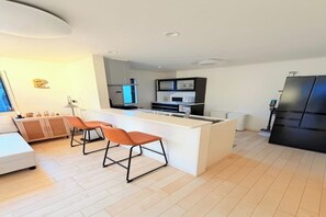 Eine moderne Küche mit Kochinsel, zwei Barhocker, einem weißen Sofa und einem Esstisch.