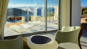 Ein modernes Zimmer mit einer großen Schiebeglasdoor, die zu einer Terrasse im Freien mit weißer Möbel und Blick aufs Meer führt.