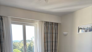 A room with two beds, a window with curtains, a small table, and a wall-mounted light fixture. - Bay view Cavalaire sur Mer - Pretty T3 Air-conditioned Top floor Swimming pool Classified **** (Cavalaire sur Mer)