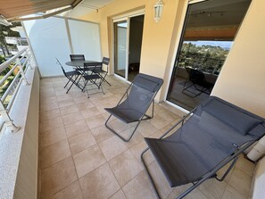 Ein Balkon mit zwei Loungestühlen, einem Tisch und Stühlen.