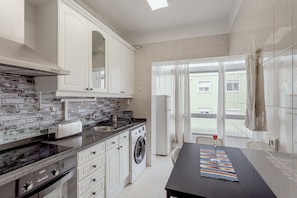Una cocina moderna con protector mural de ladrillo, armarios blancos, lavadora integrada y un comedor con mesa y sillas.