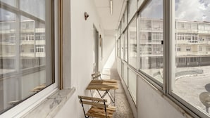 Un pasillo con amplias ventanas, una mesa de madera y sillas, que conduce a un edificio con balcones.
