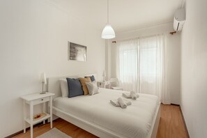 Habitación de hotel ordenada con cama, mesita de noche, lámpara y aire acondicionado instalado en la pared.