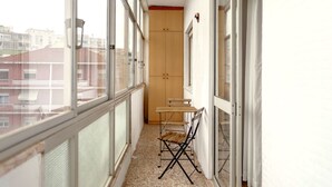 Un balcón estrecho con una silla de madera, una mesita y un armario.