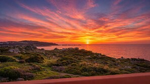 A coastal landscape with a sunset, rocky terrain, and a path leading towards the sea. - Casa Audrey by Wonderful Italy (Santa Teresa di Gallura)