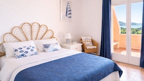 A bedroom with a bed, a chair, a nightstand, and a view of the outdoors. - Casa Audrey by Wonderful Italy (Santa Teresa di Gallura)