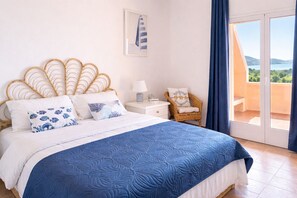 A bedroom with a bed, a chair, a nightstand, and a view of the outdoors. - Casa Audrey by Wonderful Italy (Santa Teresa di Gallura)