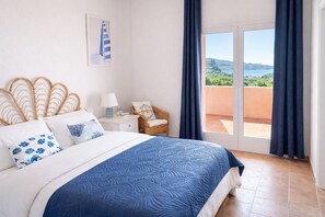 A bedroom with a bed, a nightstand, a chair, and a view of the outdoors. - Casa Audrey by Wonderful Italy (Santa Teresa di Gallura)