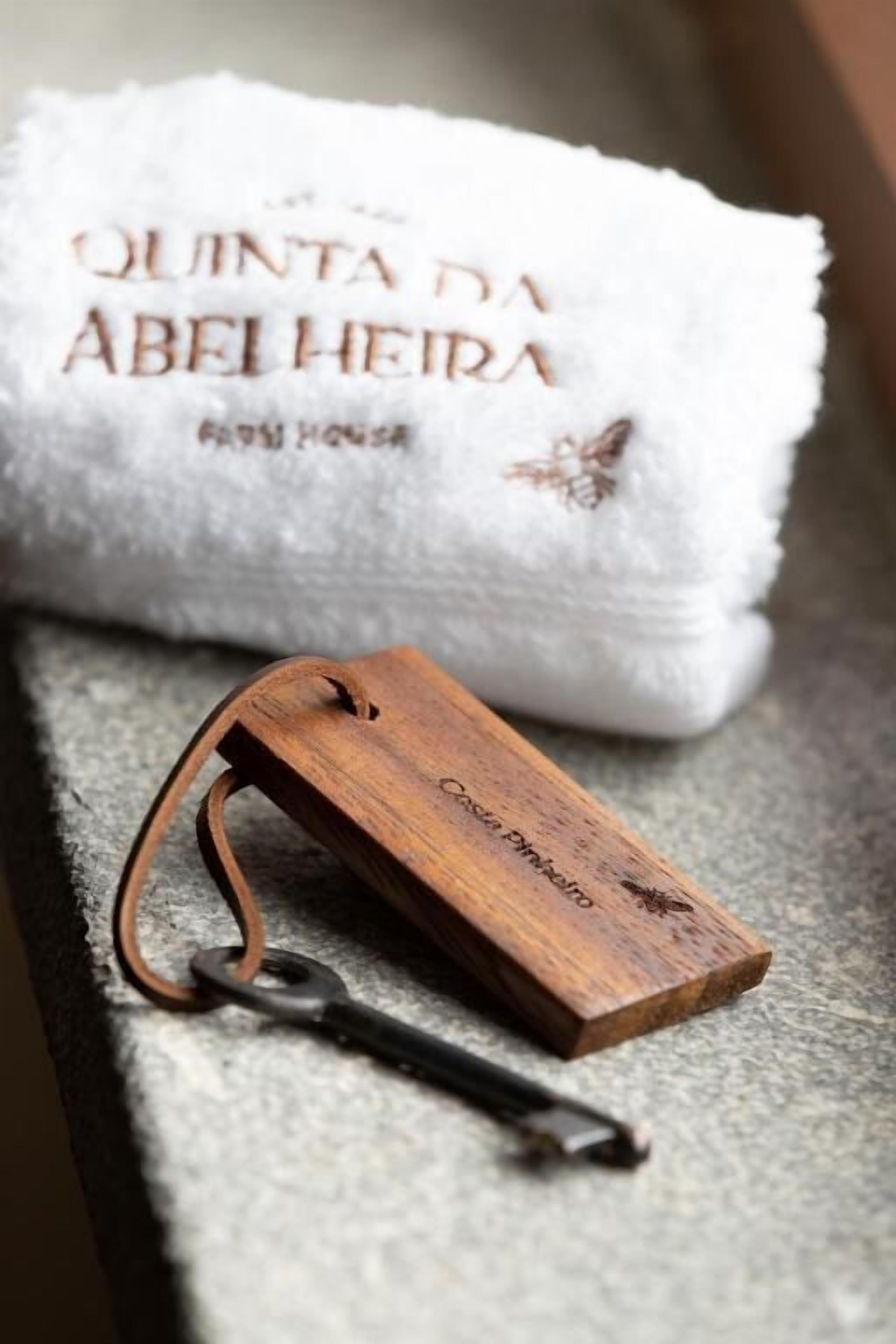 Un llavero de madera con una etiqueta, una toalla blanca con texto bordado y una superficie de piedra.
