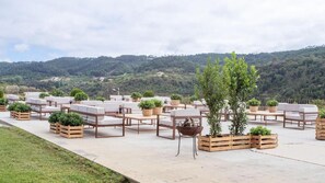 An outdoor seating area with wooden furniture and planters, set against a backdrop of hills. - Quinta da Abelheira 1660 (Mafra)
