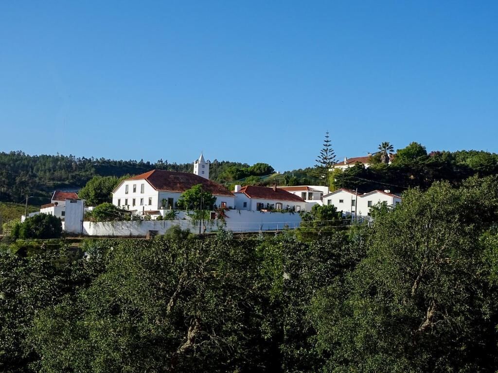Uma aldeia situada numa encosta, com edifícios brancos, uma igreja e vegetação densa.