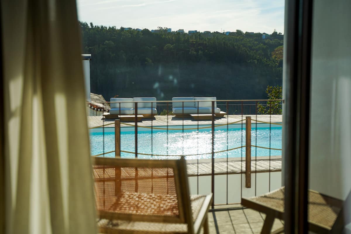 En vy över en pool med solstolar och ett trädäck, med utsikt över ett skogsområde.
