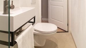 A small bathroom with a toilet, sink, and glass shower enclosure. - SAYŌ Boutique Hotel (The Hague)