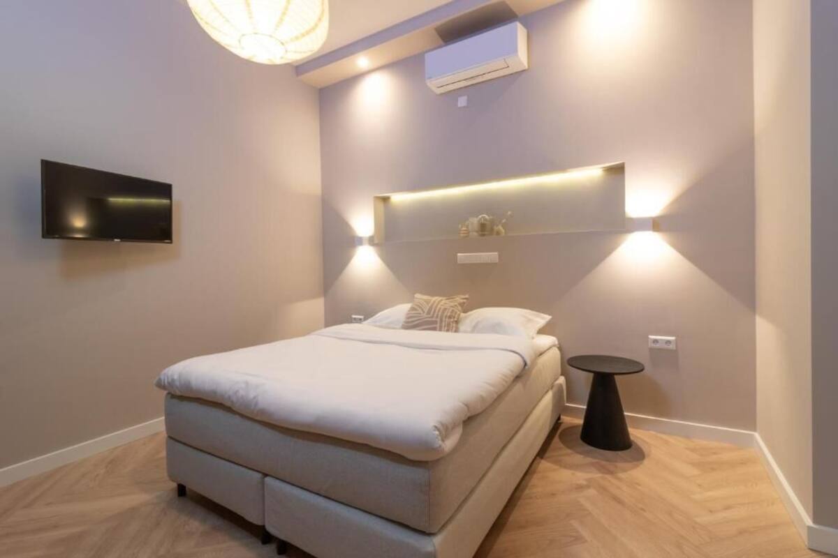 A modern bedroom with a bed, a mounted TV, an air conditioning unit, and a bedside table.