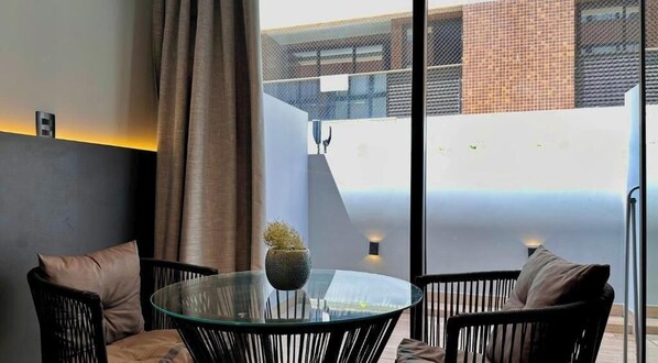 A modern outdoor seating area with a glass table, black wicker chairs, and a potted plant. - Setai Edition - LikeHome  (João Pessoa)
