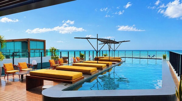 A rooftop infinity pool with yellow loungers and a glass balustrade overlooking the ocean. - Setai Edition - LikeHome  (João Pessoa)