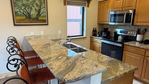 Eine Küche mit Granit Arbeitsplatten, Holzschränken, einer Edelstahl-Mikrowelle und einem Fenster mit Jalousien.