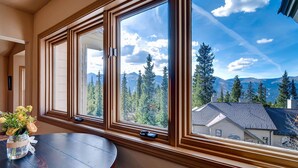 A room with large windows offering a mountain view, a round wooden table, and a vase with flowers. - Huge Views|Free Shuttle 1/2 Block|Wood Fireplace (Breckenridge)