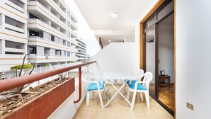 Ein Balkon mit weißem Tisch und Stühlen, Blick auf ein mehrgeschossiges Gebäude und Geländer aus Holz.