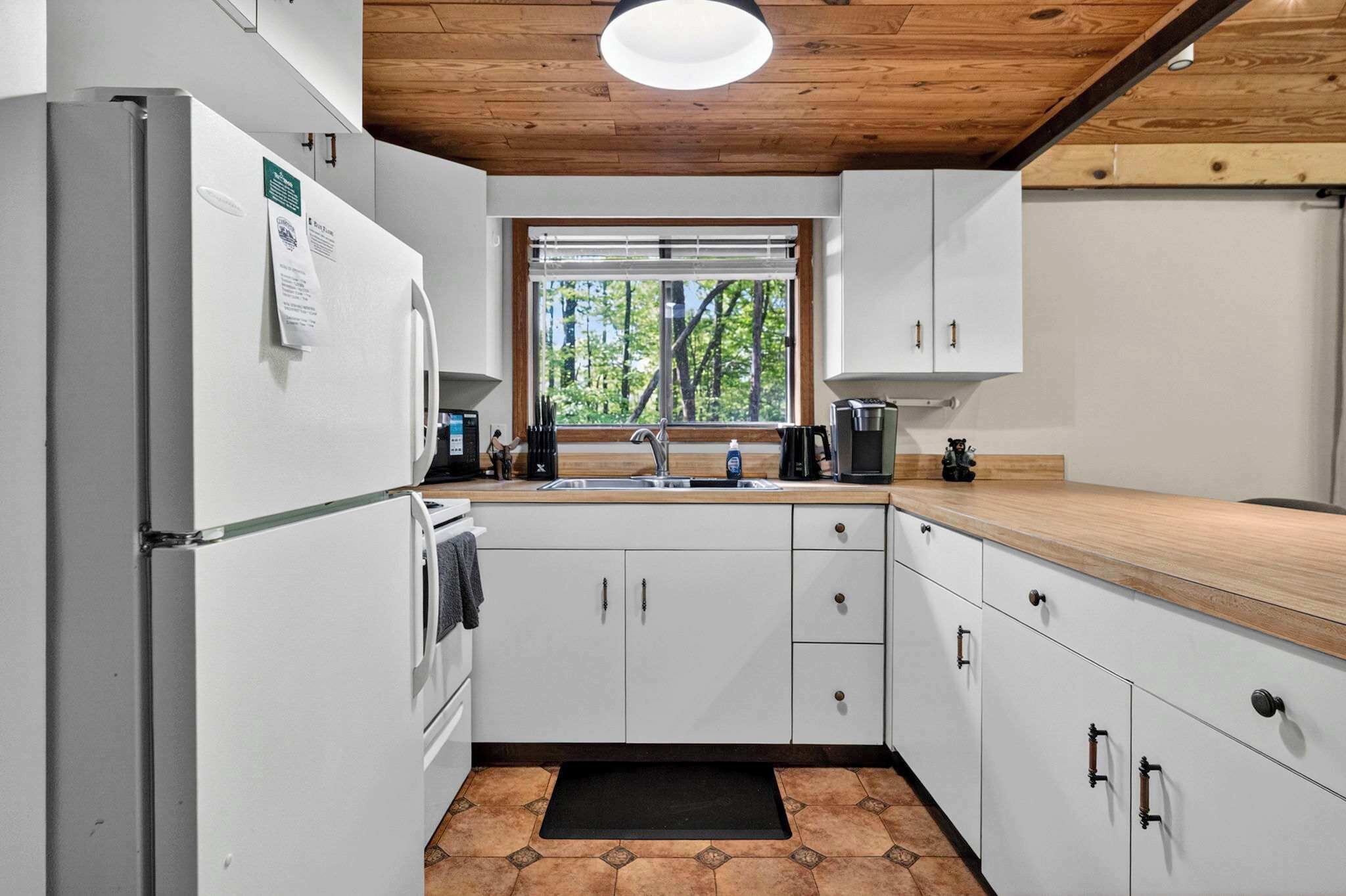 A modern kitchen with white cabinets, a wooden countertop, and a window with a view of trees.