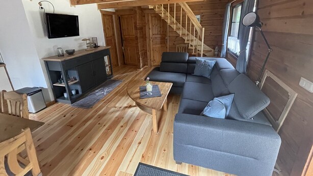 Interior de una cabaña de madera con sofá, televisor, escalera y piso de madera.