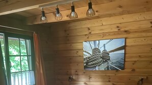Una habitación tipo cabaña de madera con una cama, una ventana con cortinas y un cuadro colgado en la pared.