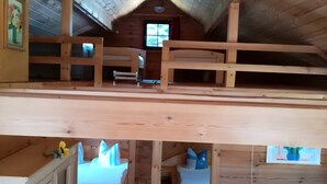 Una cabaña de madera con habitación en el altillo, un sofá y un ventanal con vistas.