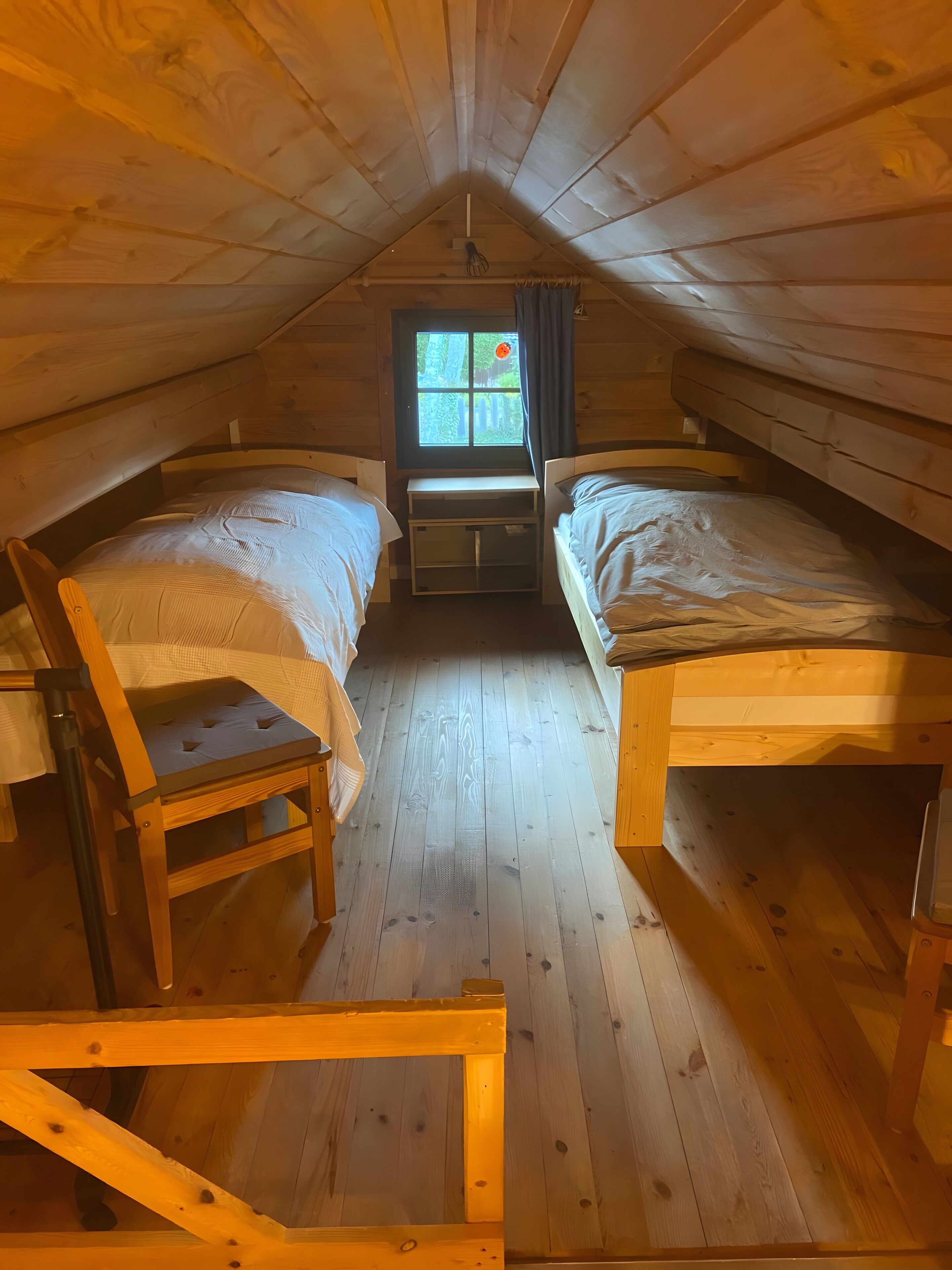 A dormitory room with two beds, a window, a chair, and a desk.