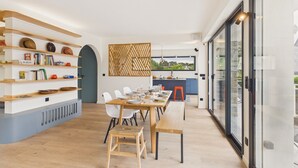 Un'area pranzo moderna con un lungo tavolo di legno, sedie bianche e una libreria con diversi oggetti.