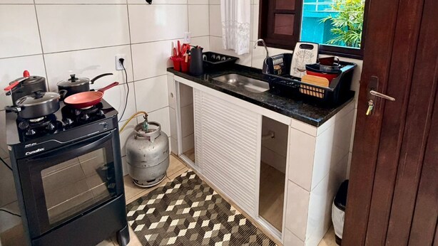 Une cuisine compacte équipée d’une cuisinière à gaz, d’un four et d’une bouteille de gaz, d’un petit plan de travail avec un évier et d’une fenêtre donnant sur un espace verdoyant.