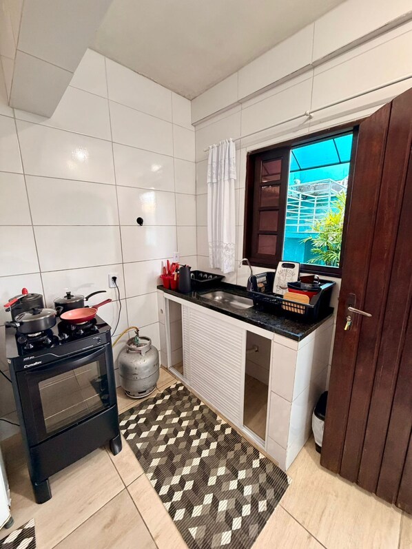 Cocina compacta con estufa a gas, horno y cilindro de gas, un mostrador pequeño con pileta y una ventana con vista a la vegetación.
