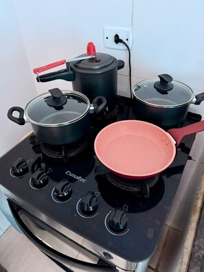 Una estufa de cocina con cuatro ollas y una sartén, un mango rojo y un enchufe.