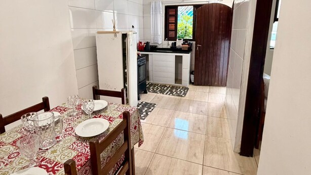 A dining area with a table set for four, a kitchen in the background, and a tiled floor. - Pousada Villa Caiçara (Ubatuba)