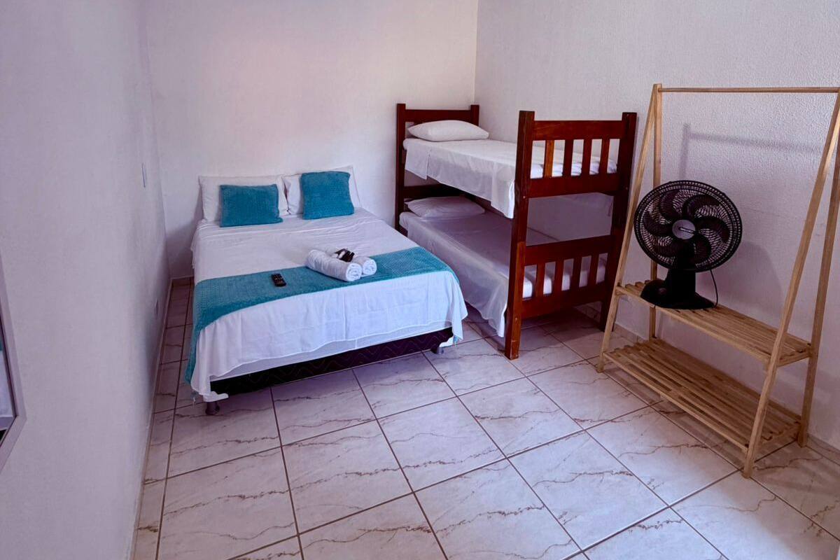 A small, clean room with a bed, a chair, a fan, and a ceiling fan.