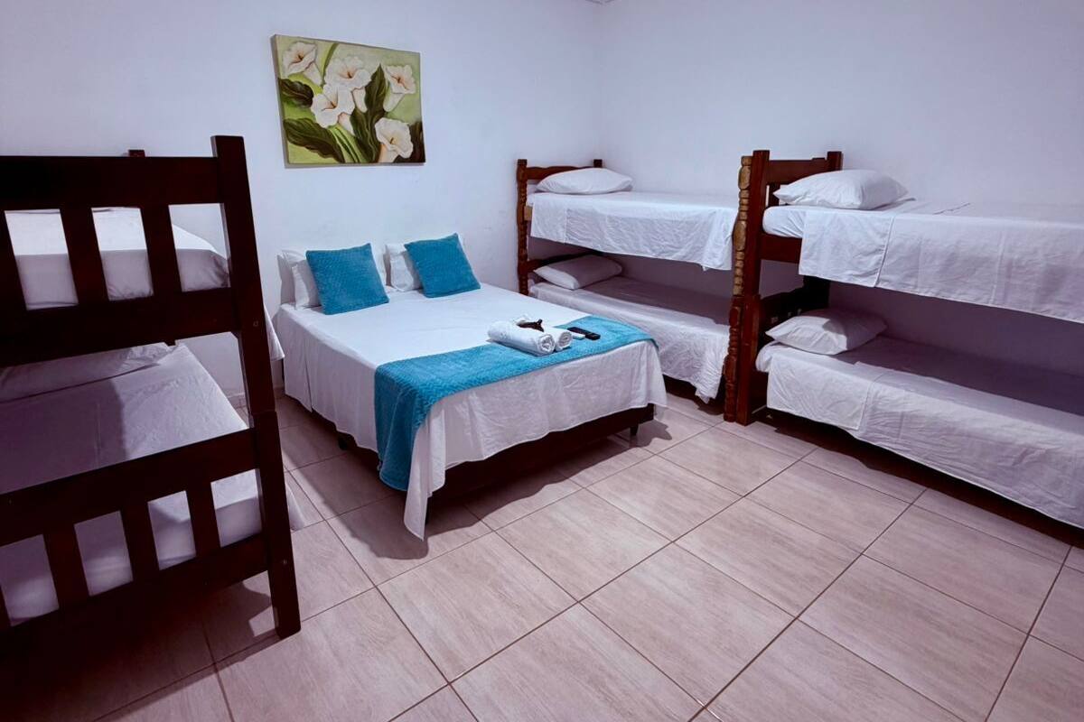 A room with bunk beds, a single bed, a painting on the wall, and a ceiling light.
