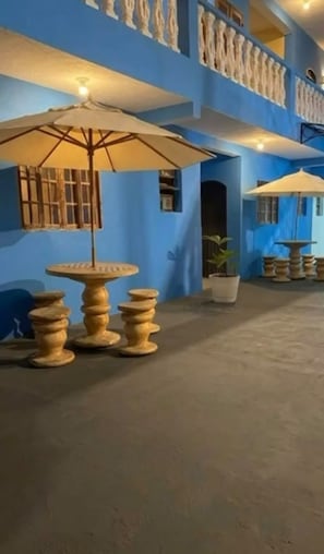 A courtyard with a round table and chairs, umbrellas, and a potted plant. - Pousada Villa Caiçara (Ubatuba)