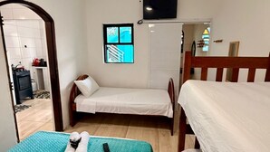 A room with two beds, a ceiling fan, a TV, and a window with a view of the outside. - Pousada Villa Caiçara (Ubatuba)