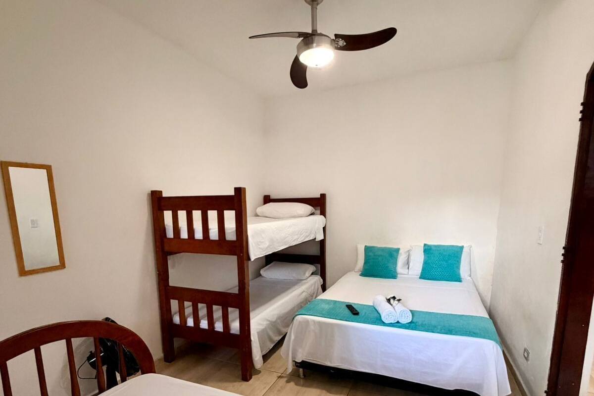 A bedroom with a bunk bed, a single bed, a ceiling fan, a wooden chair, and a bedside table.