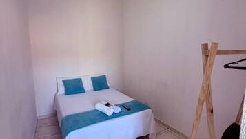 Una habitación pequeña y limpia con cama, ventilador de techo y un perchero de madera.
