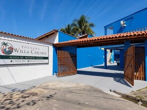 A villa with a blue facade, a gated entrance, and a signboard advertising the property. - Pousada Villa Caiçara (Ubatuba)