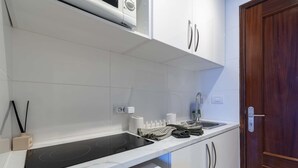 Eine moderne Küche mit integriertem Mikrowellenherd, Spüle und Herd. Über der Arbeitsfläche befinden sich Schränke und rechts eine Holztür.