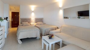 Ein Hotelzimmer mit zwei Betten, einem Schlafsofa, einem kleinen Tisch mit Obst, einem Fernseher und einem Spiegel.