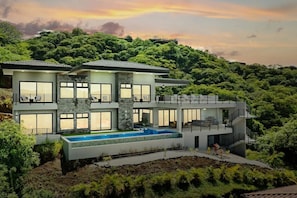 Ein modernes, zweistöckiges Haus mit Swimmingpool, umgeben von üppiger Vegetation.