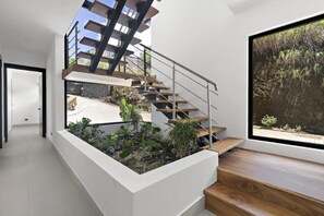 Eine moderne Treppe mit Glastrennwand, die zu einem Balkon mit Pflanzen und Blick auf einen Garten führt.