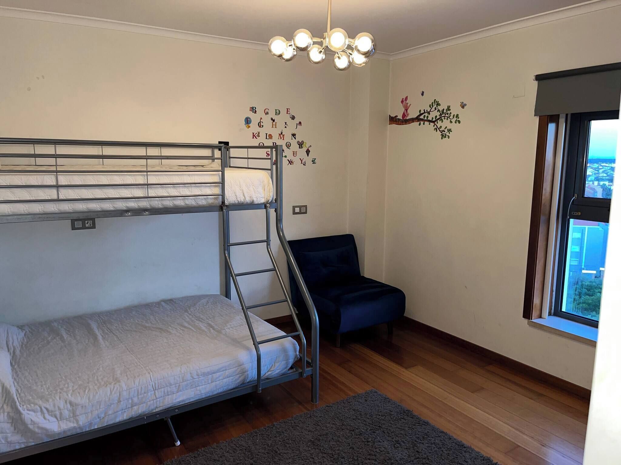 A bunk bed room with a ladder, a blue chair, a wall decoration, and a window.