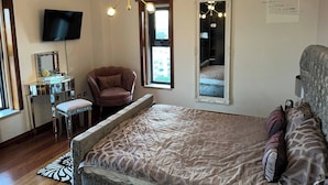 A bedroom with a bed, a chair, a vanity with a mirror, a television, a chandelier, and a window. - Luxury Apartment, Near Beach&golf (Seixal)