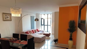 A modern living room with a sofa, dining table, chairs, and a large window. - Luxury Apartment, Near Beach&golf (Seixal)